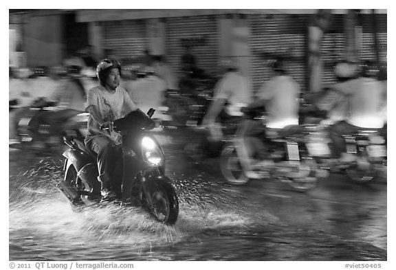 Man riding motorbike on flooded street seen against riders going in opposite direction. Ho Chi Minh City, Vietnam (black and white)