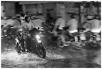 Man riding motorbike on flooded street seen against riders going in opposite direction. Ho Chi Minh City, Vietnam (black and white)