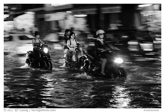 Women riding motorcyles at night in water. Ho Chi Minh City, Vietnam (black and white)