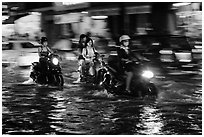 Women riding motorcyles at night in water. Ho Chi Minh City, Vietnam (black and white)