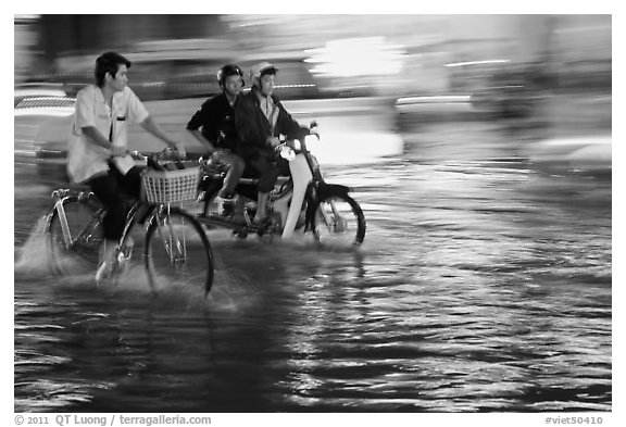 Bicyle and motorbike riders on monsoon-flooded street. Ho Chi Minh City, Vietnam (black and white)