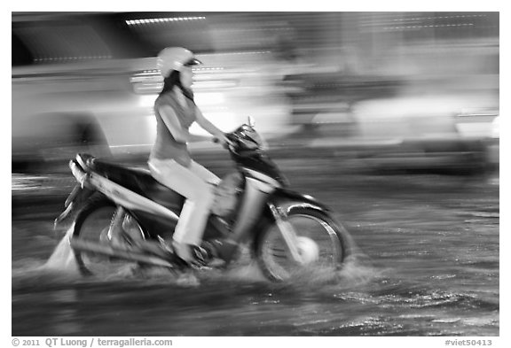 Woman riding on water-filled street, and light streaks. Ho Chi Minh City, Vietnam