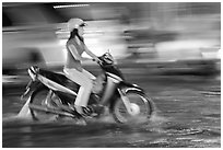 Woman riding on water-filled street, and light streaks. Ho Chi Minh City, Vietnam (black and white)