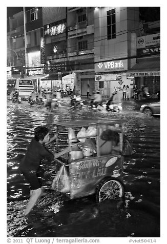 Vendor pushing foot car into the water at night. Ho Chi Minh City, Vietnam (black and white)