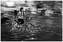 Girls sharing night bicycle ride through water of flooded street. Ho Chi Minh City, Vietnam (black and white)