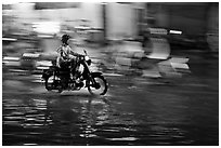 Motorcyclist speeding on wet street at night, with streaks giving sense of motion. Ho Chi Minh City, Vietnam (black and white)