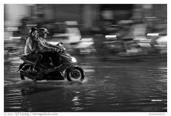 Couple sharing fast night ride on wet street. Ho Chi Minh City, Vietnam (black and white)