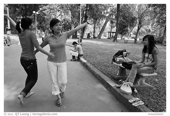 Young women dancing to sound of mobile phone, Tao Dan Park. Ho Chi Minh City, Vietnam (black and white)