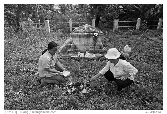 Women burning notes as offering in cemetery. Ben Tre, Vietnam (black and white)