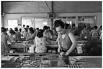 Woman cutting strips of coconut candy in factory. Ben Tre, Vietnam (black and white)