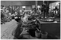 Woman feeding furnace in cococut candy factory. Ben Tre, Vietnam (black and white)