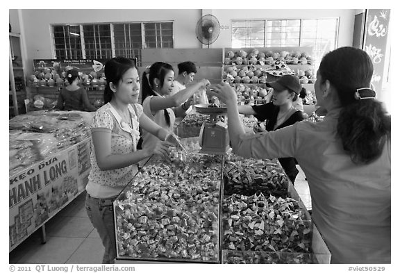 Women weighting coconut candy in retail store. Ben Tre, Vietnam (black and white)