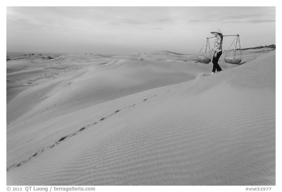 Woman descending sandhill with pannier baskets. Mui Ne, Vietnam (black and white)