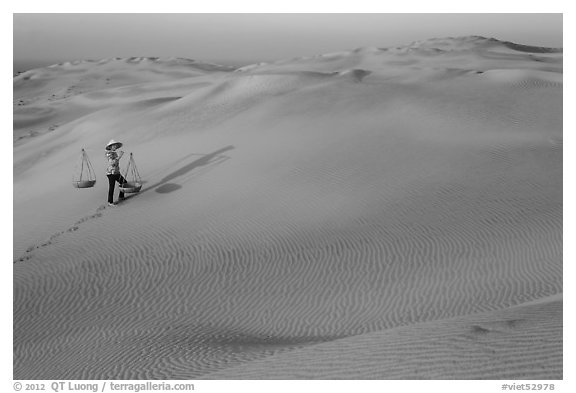 Red sand dunes and woman with carrying pole and baskets. Mui Ne, Vietnam (black and white)