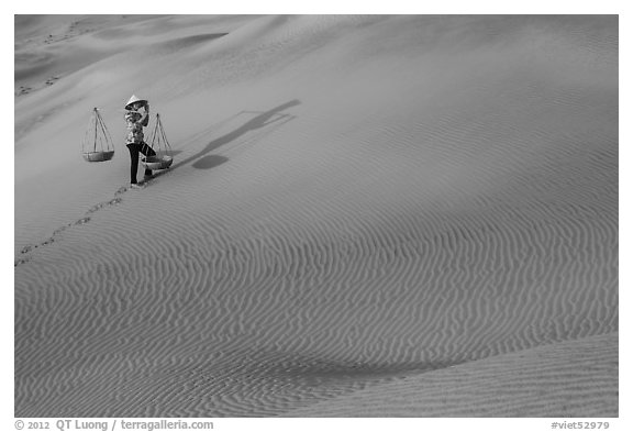 Woman walking with baskets on sands. Mui Ne, Vietnam