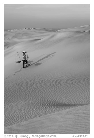 Rippled red sand dunes and woman with baskets. Mui Ne, Vietnam (black and white)