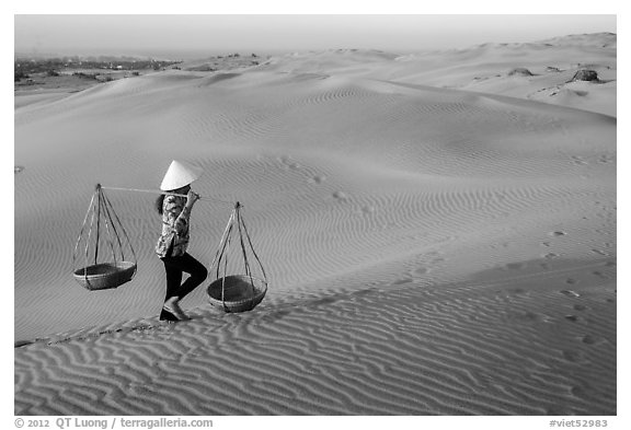 Woman carrying two baskets on shoulder pole. Mui Ne, Vietnam (black and white)