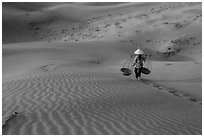 Woman with conical hat carries pannier baskets. Mui Ne, Vietnam (black and white)