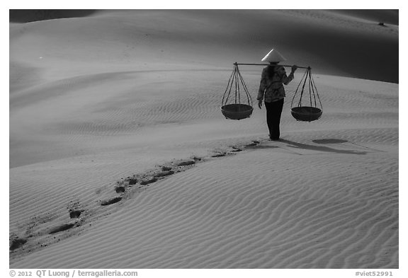 Woman walking on sand with two shoulder baskets. Mui Ne, Vietnam