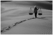 Woman walking on sand with two shoulder baskets. Mui Ne, Vietnam (black and white)