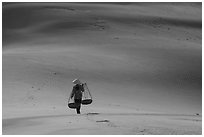 Woman walking on dune field with yoke baskets. Mui Ne, Vietnam (black and white)