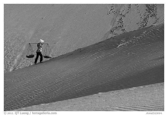 Woman ascending dune ridge with two baskets. Mui Ne, Vietnam (black and white)