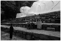 Woman prays below reclining Buddha statue. Ta Cu Mountain, Vietnam (black and white)