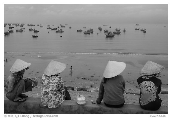 Four women in conical hats watch fishing activity from high above fishing village. Mui Ne, Vietnam (black and white)