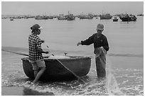 Man and woman gathering fishing net onto roundboat. Mui Ne, Vietnam (black and white)