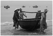 Fishermen carry round woven boat to shore. Mui Ne, Vietnam (black and white)