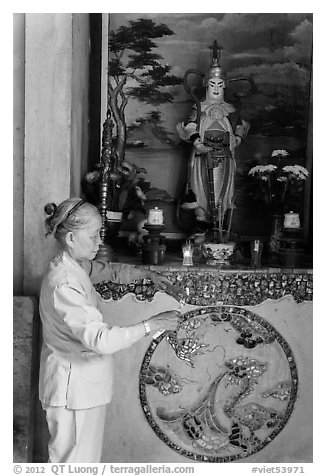 Woman lighting incense at side altar. Da Nang, Vietnam (black and white)