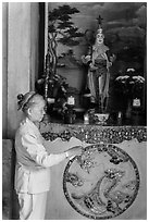 Woman lighting incense at side altar. Da Nang, Vietnam (black and white)