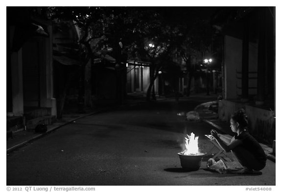 Woman burning paper on street at night. Hoi An, Vietnam