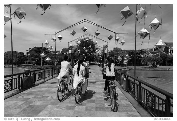 Girls on bicycle cross bridge festoned with lanterns. Hoi An, Vietnam (black and white)