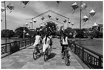 Girls on bicycle cross bridge festoned with lanterns. Hoi An, Vietnam (black and white)