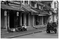 Man pulling cart in front of old townhouses. Hoi An, Vietnam ( black and white)