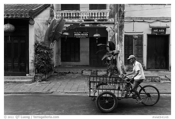 Man riding tricycle cart in front of old townhouses. Hoi An, Vietnam (black and white)