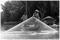 Fisherman pulls up net from rowboat. Hoi An, Vietnam ( black and white)