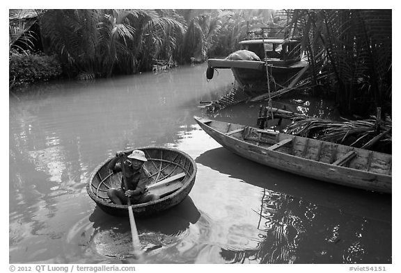 Man rows coracle boat in river channel. Hoi An, Vietnam (black and white)