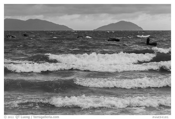 Man rowing coracle boat in distance amidst large waves. Da Nang, Vietnam (black and white)