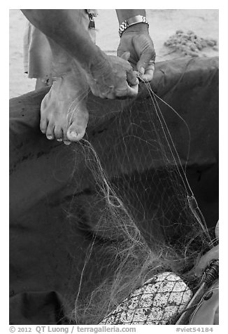 Close-up of hands and feet of man mending net. Da Nang, Vietnam (black and white)