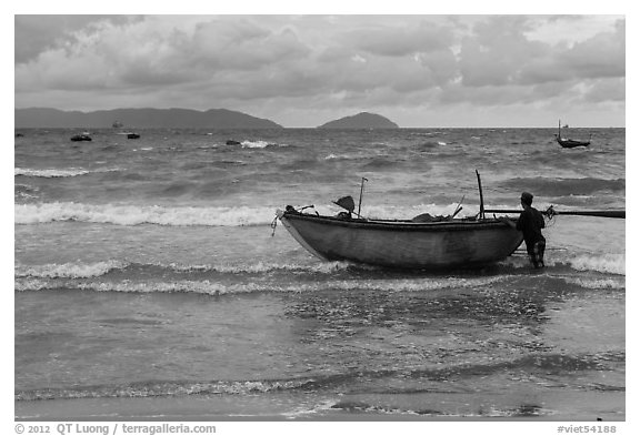 Man entering ocean with boat in stormy weather. Da Nang, Vietnam (black and white)