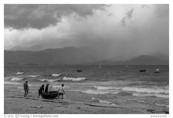 Men pushing coracle boat into stormy ocean. Da Nang, Vietnam (black and white)