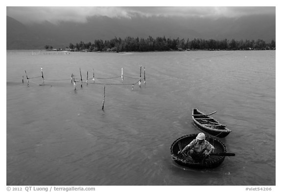 Man rowing coracle boat in lagoon. Vietnam (black and white)