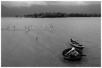 Man rowing coracle boat in lagoon. Vietnam (black and white)