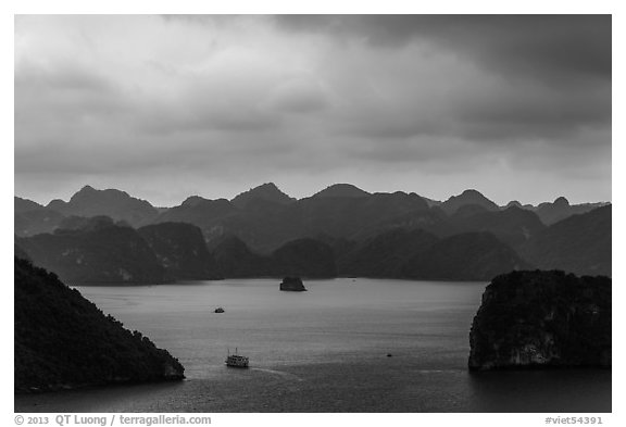 Boat amongst islands under dark sky. Halong Bay, Vietnam (black and white)