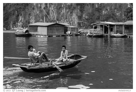 Man holding infant while rowing with feet, Vung Vieng village. Halong Bay, Vietnam (black and white)