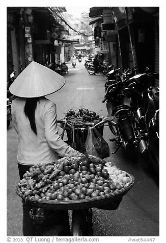 Woman pushing bicycle loaded with vegetable for sale in narrow street, old quarter. Hanoi, Vietnam (black and white)