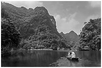 Boat journeying below tall lush cliffs, Trang An. Ninh Binh,  Vietnam (black and white)