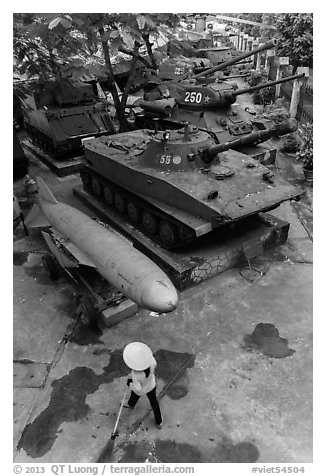 Woman sweeping floor in front of military hardware, military museum. Hanoi, Vietnam (black and white)